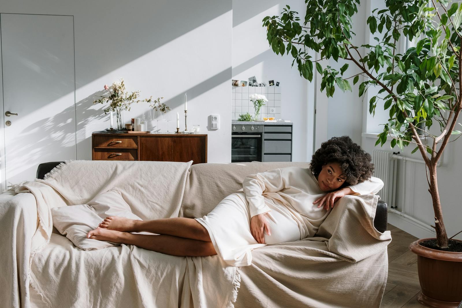 Pregnant woman relaxing on a sofa in a warm, Scandinavian-style living room, bathed in natural light.